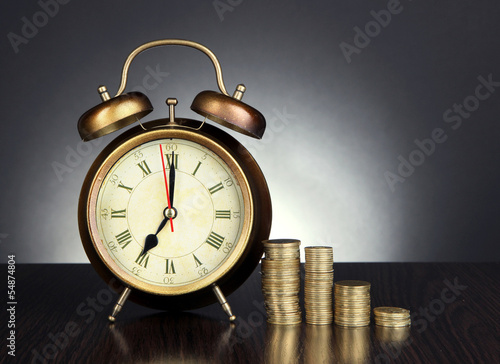 Photo: Antique clock and coins on wooden table on black background Antique clock and coins on wooden table on black background