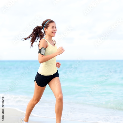 Photo: Running woman jogging on beach listening to music Running woman jogging on beach listening to music