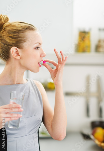 Photo: Young woman eating pill in kitchen Young woman eating pill in kitchen