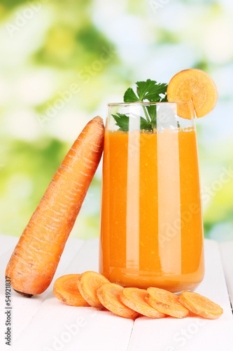 Photo: Glass of carrot juice on wooden table, on green background Glass of carrot juice on wooden table, on green background