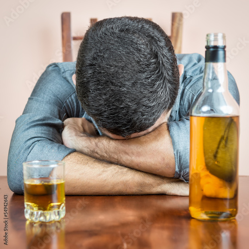 Photo: Drunk man sleeping with a whisky bottle on his table Drunk man sleeping with a whisky bottle on his table