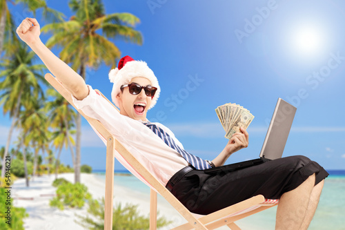 Photo: Excited man with santa hat on a beach chair holding banknotes Excited man with santa hat on a beach chair holding banknotes