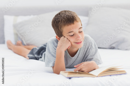 Photo: Little boy lying on bed reading book Little boy lying on bed reading book