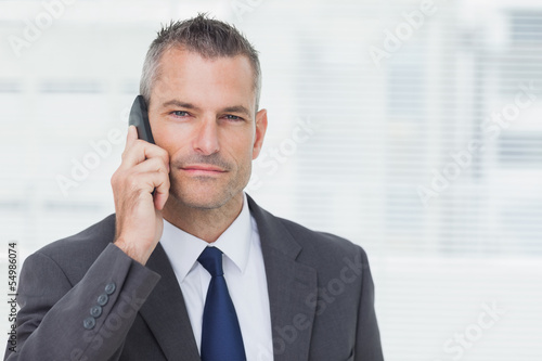 Photo: Businessman looking at camera while having a phone call Businessman looking at camera while having a phone call