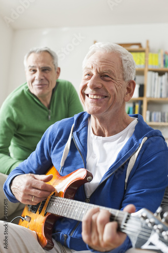 Photo: Deutschland, Leipzig, Senior, Rentner spielt E-Gitarre, Mann sitzt im Hintergrund Deutschland, Leipzig, Senior, Rentner spielt E-Gitarre, Mann sitzt im Hintergrund