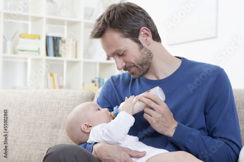 Photo: Deutschland, Bayern, München, Vater Fütterung Milch Baby im Wohnzimmer Deutschland, Bayern, München, Vater Fütterung Milch Baby im Wohnzimmer