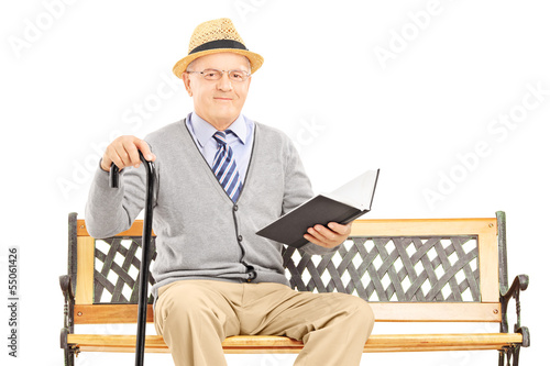 Photo: Senior man sitting on a wooden bench and reading a book Senior man sitting on a wooden bench and reading a book