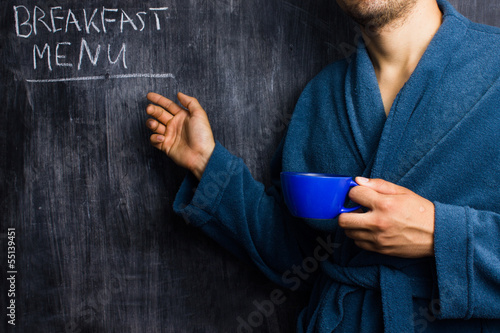 Photo: Man in robe pointing at breakfast menu on blackboard Man in robe pointing at breakfast menu on blackboard