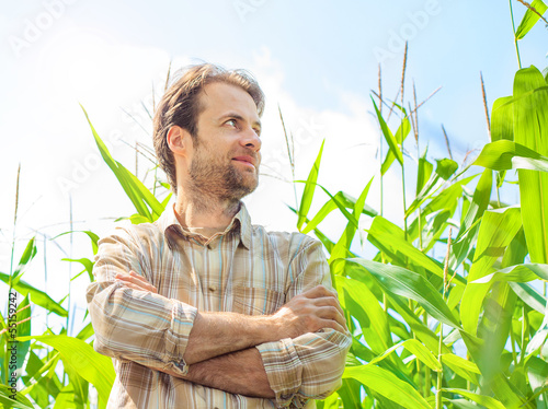 Photo: Happy smiling caucasian farmer in front of corn field Happy smiling caucasian farmer in front of corn field