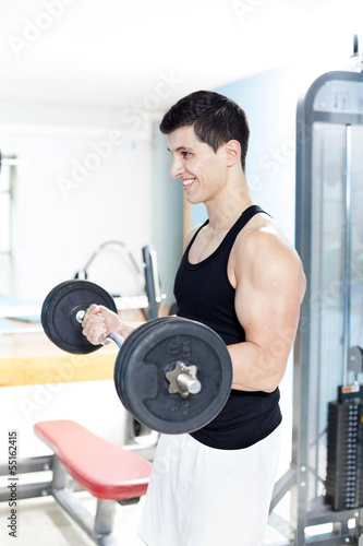 Photo: Smiling handsome man lifting heavy free weights at the gym Smiling handsome man lifting heavy free weights at the gym