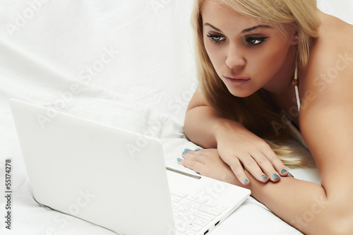 Photo: beautiful blond girl on bed with laptop. beauty woman. white beautiful blond girl on bed with laptop. beauty woman. white