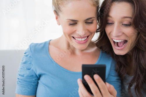 Photo: Cheerful friends reading message on their phone Cheerful friends reading message on their phone
