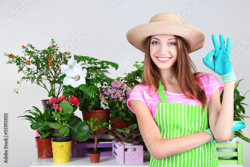 Photo: Beautiful girl gardener with flowers on grey background Beautiful girl gardener with flowers on grey background