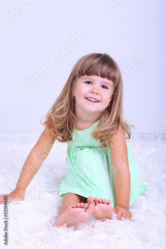 Photo: Little cute girl sitting on carpet, on gray background Little cute girl sitting on carpet, on gray background