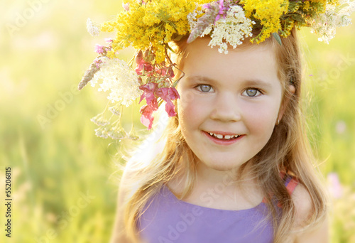 Photo: Happy little girl in flower crown on sunny summer meadow Happy little girl in flower crown on sunny summer meadow