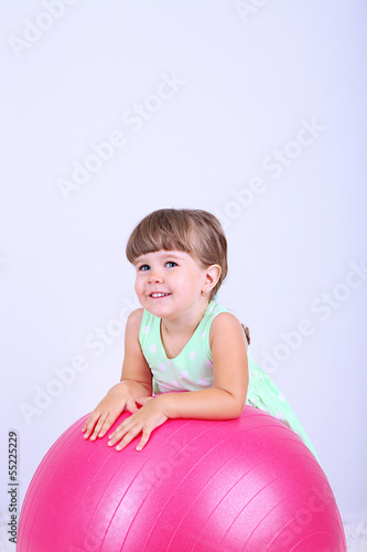 Photo: Little cute girl playing with big ball, on gray background Little cute girl playing with big ball, on gray background