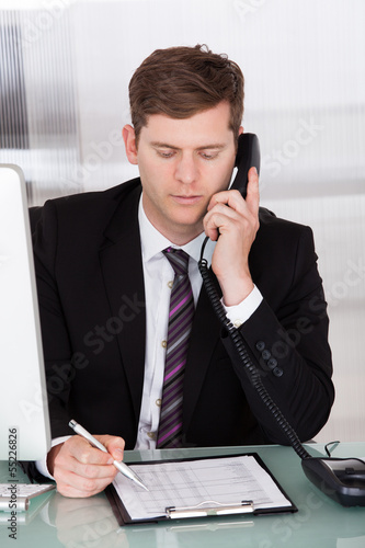 Photo: Businessman talking on telephone in office Businessman talking on telephone in office