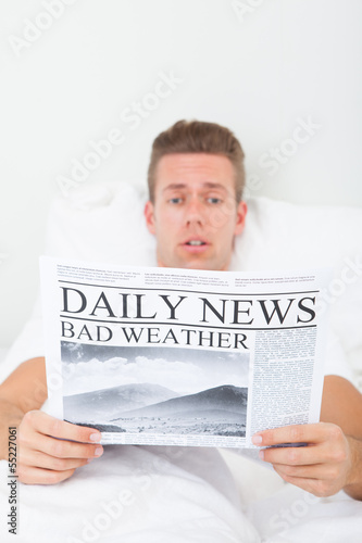 Photo: Shocked Young Man Lying On Bed Reading Newspaper Shocked Young Man Lying On Bed Reading Newspaper