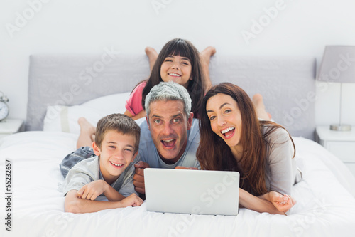 Photo: Funny family lying on bed using their laptop Funny family lying on bed using their laptop