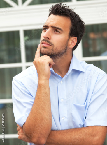 Photo: Thoughtful young businessman in front of his office Thoughtful young businessman in front of his office