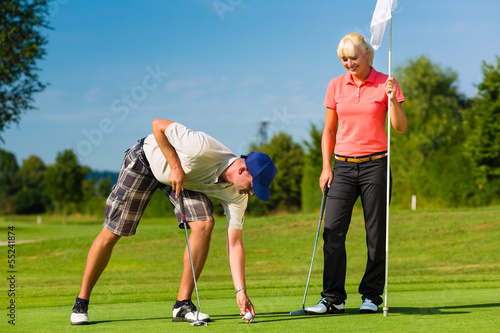 Photo: Young sportive couple playing golf on a course Young sportive couple playing golf on a course