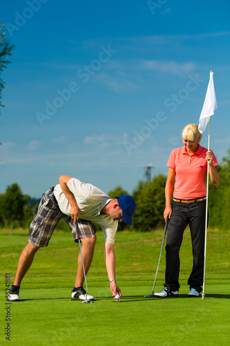 Photo: Young sportive couple playing golf on a course Young sportive couple playing golf on a course