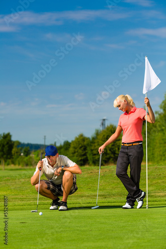 Photo: Young sportive couple playing golf on a course Young sportive couple playing golf on a course