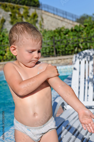 Photo: Young boy at the pool applying sunscreen Young boy at the pool applying sunscreen
