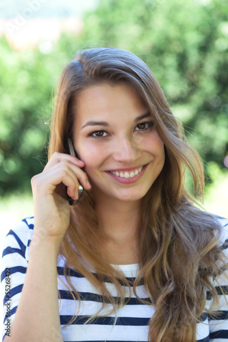 Photo: Beautiful young woman smiling on the phone in a park Beautiful young woman smiling on the phone in a park