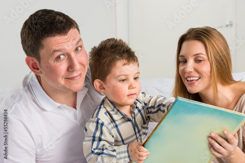 Photo: Parents Sitting With Child Reading Story Indoors Parents Sitting With Child Reading Story Indoors