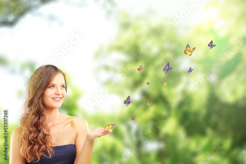 Photo: Beautiful female with a butterfly on her hand posing in a park Beautiful female with a butterfly on her hand posing in a park