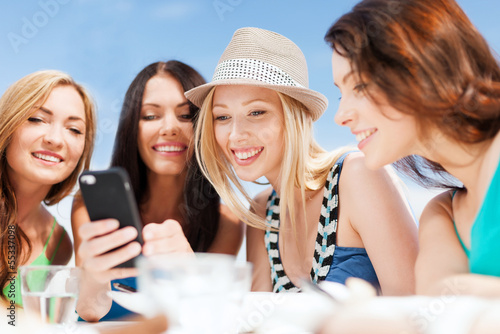Photo: girls looking at smartphone in cafe on the beach girls looking at smartphone in cafe on the beach