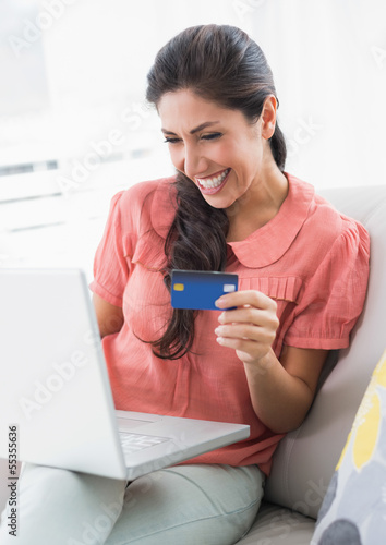 Photo: Cheerful brunette sitting on her sofa using laptop to shop onlin Cheerful brunette sitting on her sofa using laptop to shop onlin