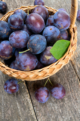 Photo: plums in basket on wooden surface plums in basket on wooden surface