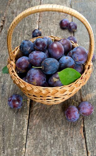 Photo: plums in basket on wooden surface plums in basket on wooden surface