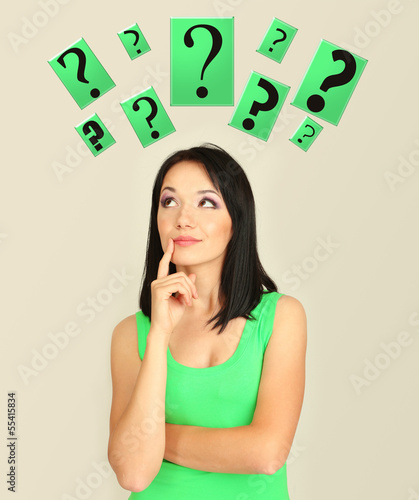 Photo: Girl thinking surrounded by question marks on beige background Girl thinking surrounded by question marks on beige background