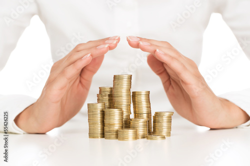 Photo: Savings protection, close up of female hands covering stack of g Savings protection, close up of female hands covering stack of g