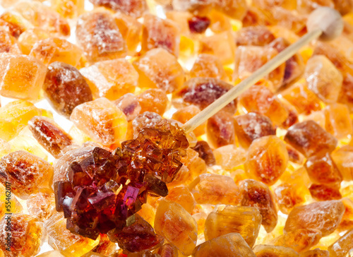 Photo: Brown candy sugar on stick on scattering of brown sugar.. Brown candy sugar on stick on scattering of brown sugar..