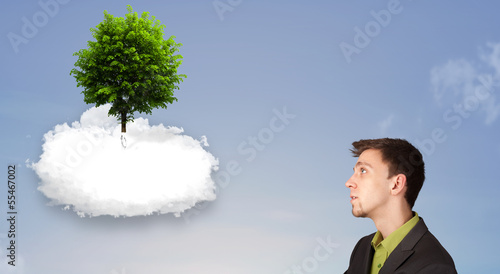 Photo: Young man pointing at a green tree on top of a white cloud Young man pointing at a green tree on top of a white cloud