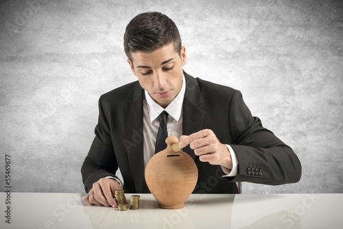 Photo: Businessman putting coin into the piggy bank Businessman putting coin into the piggy bank