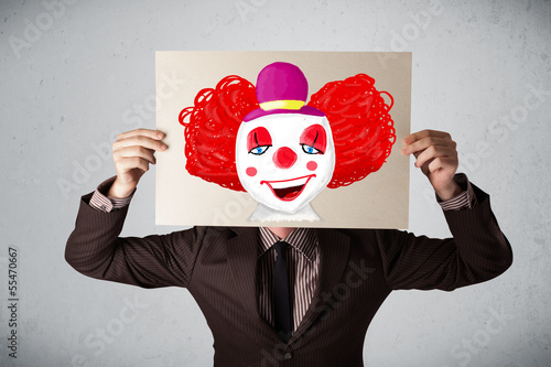Photo: Businessman holding a cardboard with a clown on it in front of h Businessman holding a cardboard with a clown on it in front of h
