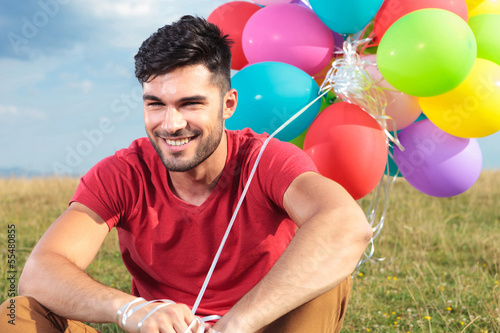 Photo: closeup of seated casual man with balloons closeup of seated casual man with balloons