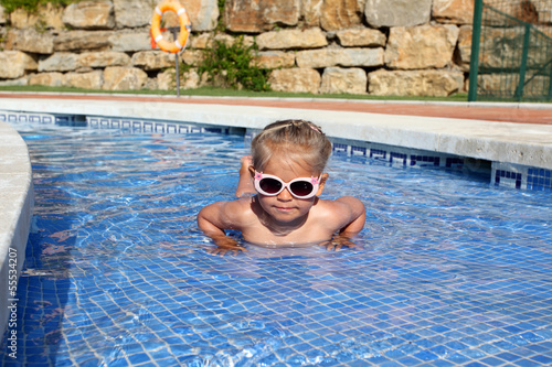 Photo: Little girl with sun glasses having fun in the pool Little girl with sun glasses having fun in the pool