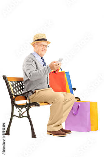 Photo: Senior man seated on a bench with shopping bags and typing a sms Senior man seated on a bench with shopping bags and typing a sms