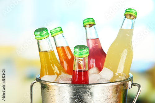 Photo: Bottles with tasty drinks in bucket with ice cubes, in bright Bottles with tasty drinks in bucket with ice cubes, in bright