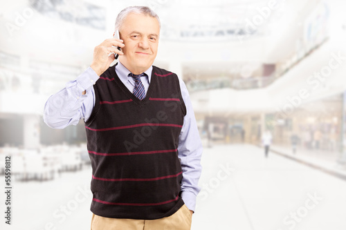 Photo: Smiling gentleman talking on a phone and posing in shopping mall Smiling gentleman talking on a phone and posing in shopping mall