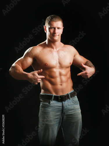 Photo: Muscular young man showing abs, isolated on black background Muscular young man showing abs, isolated on black background