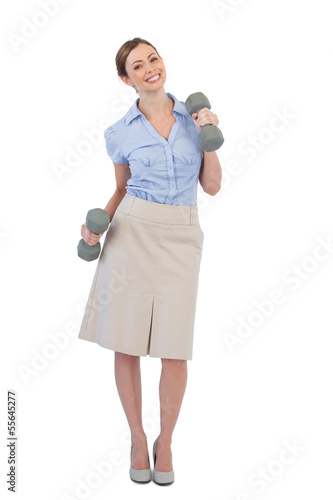 Photo: Happy businesswoman lifting dumbbells looking at camera Happy businesswoman lifting dumbbells looking at camera