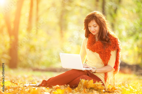 Photo: Cute woman with white laptop in the autumn park Cute woman with white laptop in the autumn park