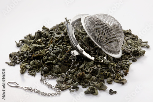 Photo: Green tea leaves and a tea strainer on white background Green tea leaves and a tea strainer on white background